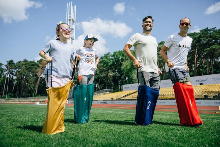 dwóch mężczyzn z dwójką dzieci skaczący w workach na stadionie lekkoatletycznym