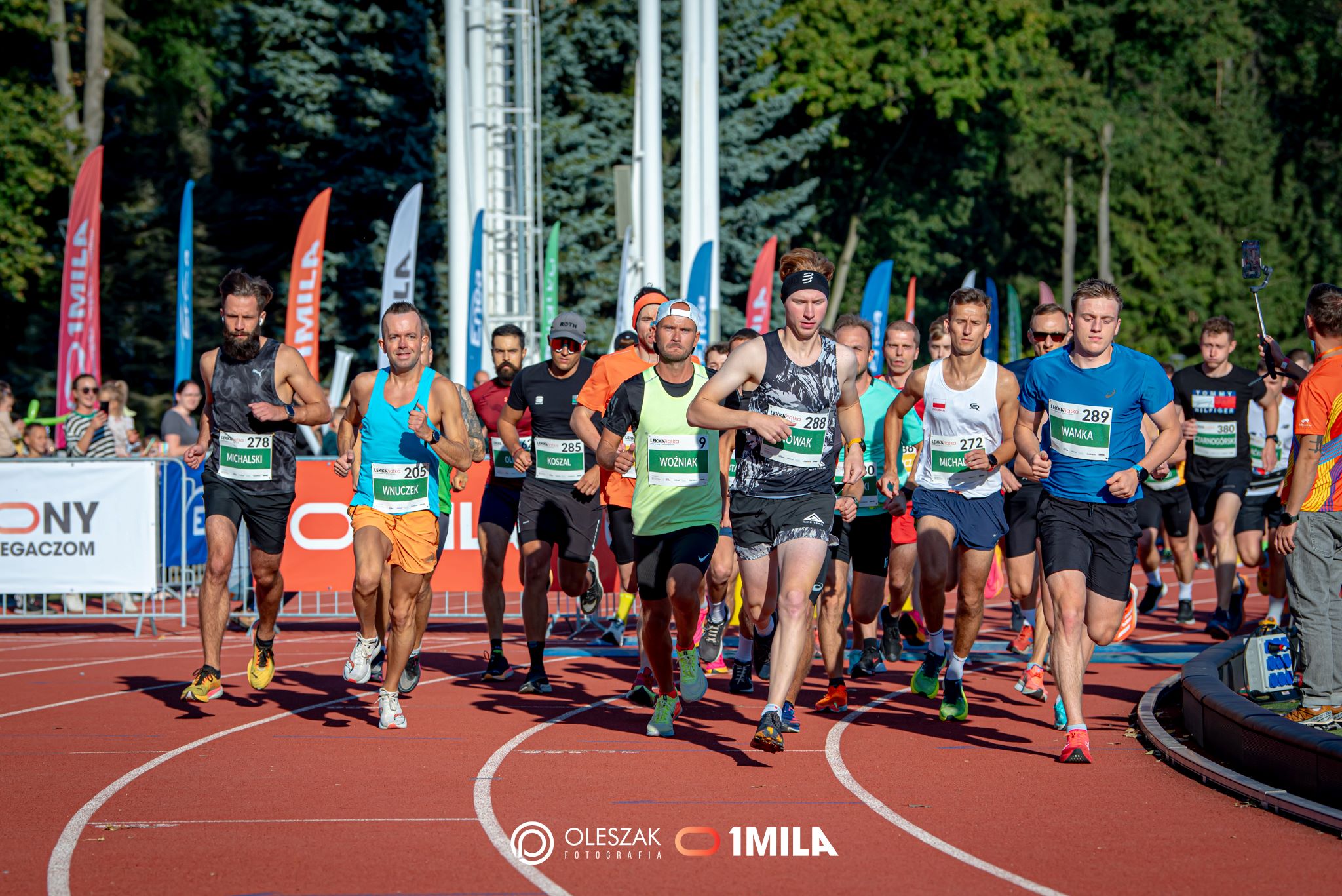 Biegacze biegną po bieżni lekkoatletycznej.