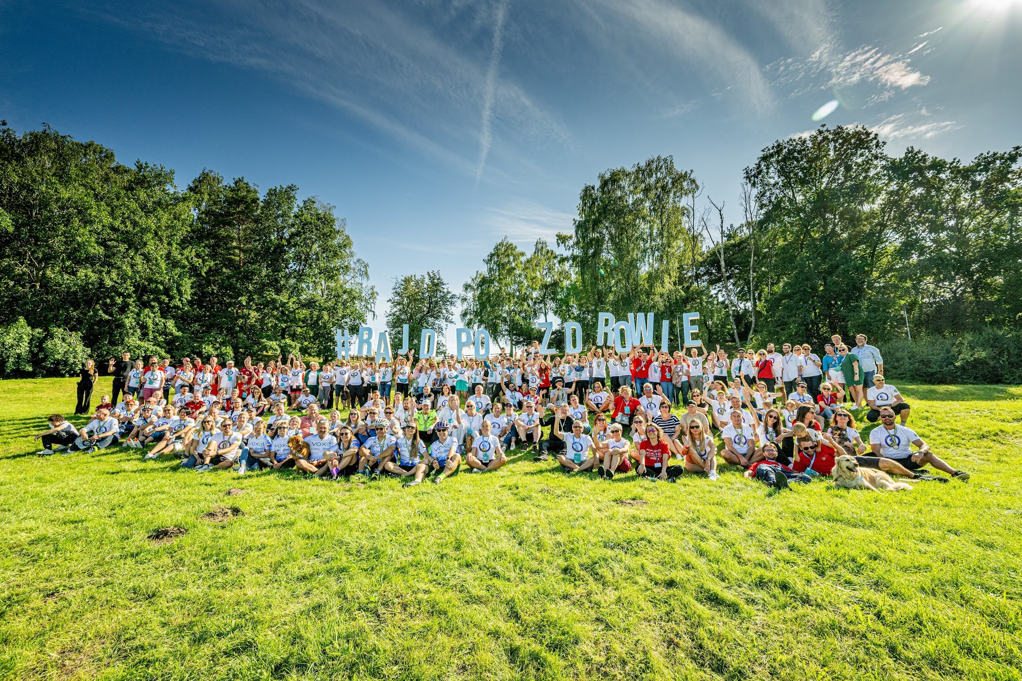 na zdjęciu widać grupę ludzi na trawie, w tyle napis #RajdPoZdrowie - zdjęcie główne