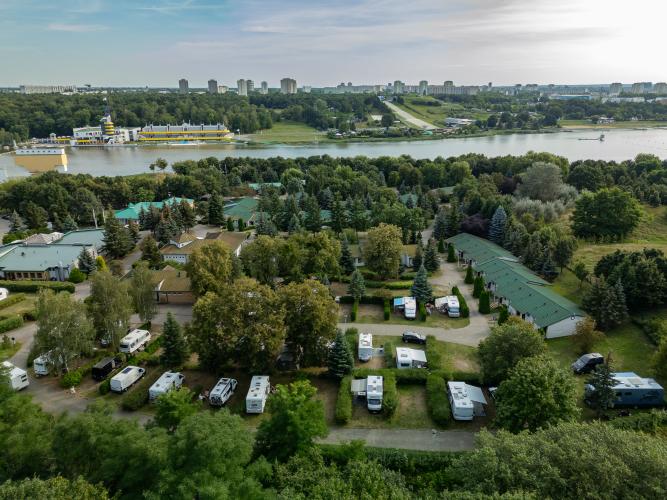 camping malta z lotu ptaka, na pierwszym planie domki, pole campingowe, zieleń. W drugim widoczne osiedle domków jednorodzinnych