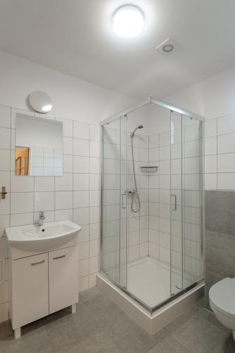 łazienka hotelow, na ścianach białe płytki, na wprost kabina prysznicowa, po prawej stronie toaleta, po lewej umywalaka na ścianie lustro