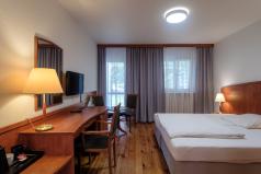 zdjęcie przedstawia pokój hotelowy, z prawej duże łóżko po lewej stroniebiurko na biurku lampa nad biurkiemna ścianie wisi lustro i telewizor