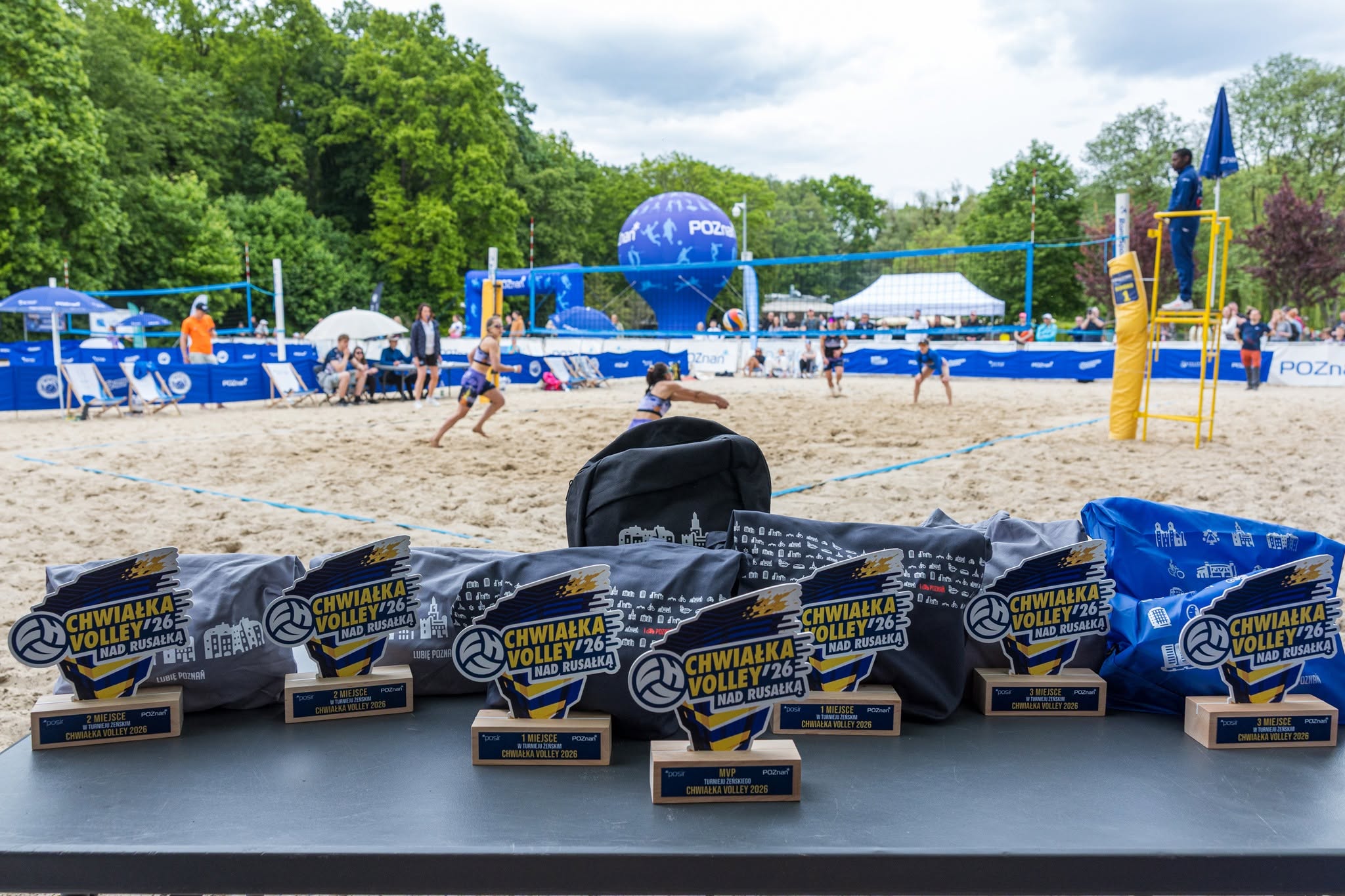 Statuetki dla zwycięzców Chwiałka Volley na tle boiska do siatkówki plażowejjpg